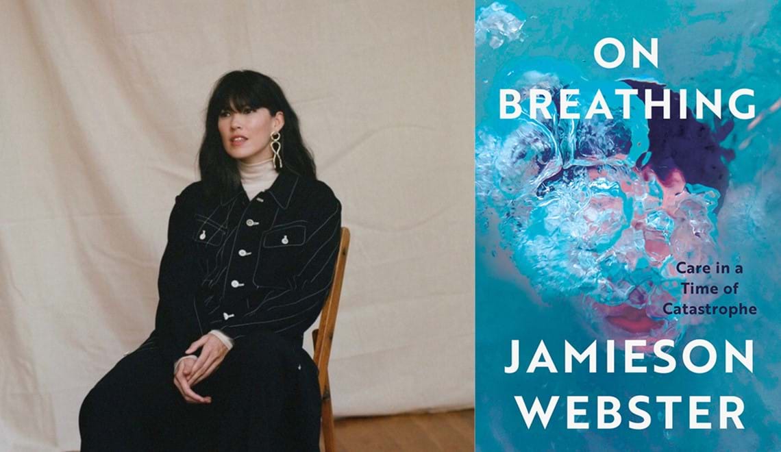Jamieson Webster sits on a wooden chair in front of a white sheet. Jamieson wears a dark jacket and skirt and has long black hair and a fringe.