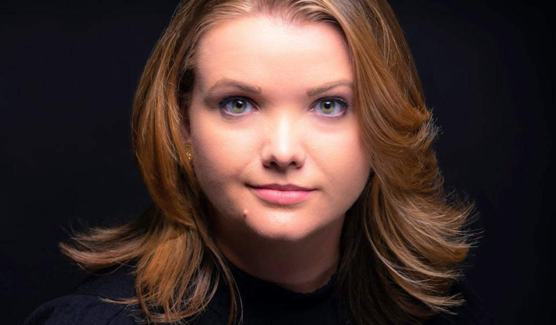 Téa Obreht has brown hair and wears a black top in front of a black background.