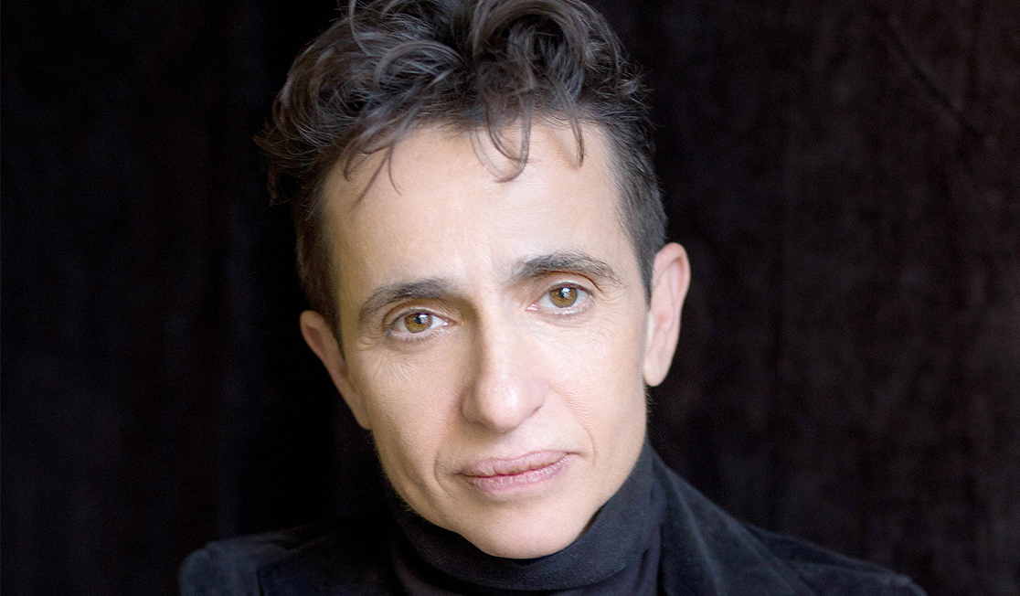 Masha Gessen wears a navy blue turtleneck under a black jacket, on a black background 