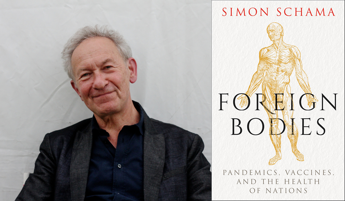 Sir Simon Schama wears a dark grey suit jacket and a navy shirt. Simon has short grey hair and smiles in front of a white background.