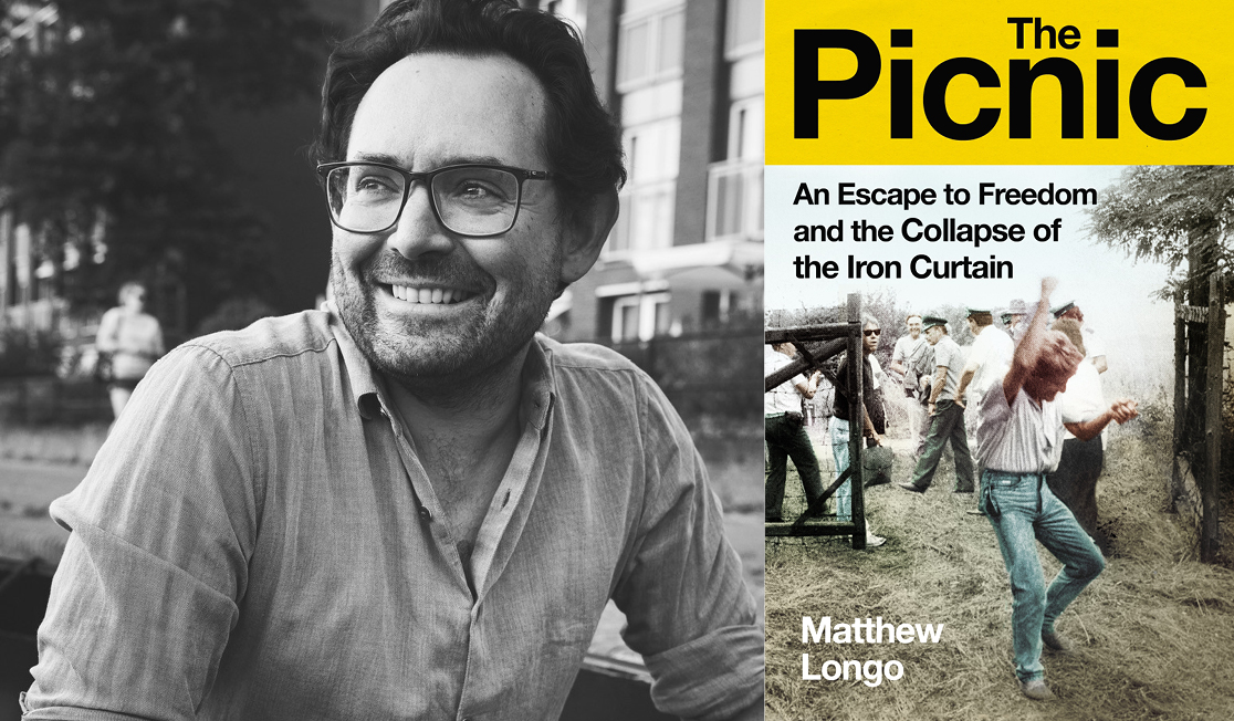 Matthew Longo wears a light shirt and dark framed glasses. He has short dark hair and a beard. He is sitting outdoors and smiling.