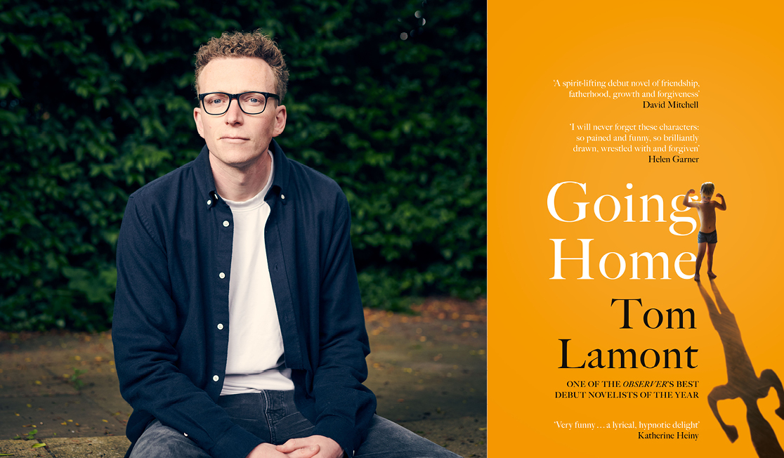 Tom Lamont sits outside in front of green foliage. Tom wears a blue shirt with the white tee and dark frame glasses. Tom has short brown hair and is slightly smiling.