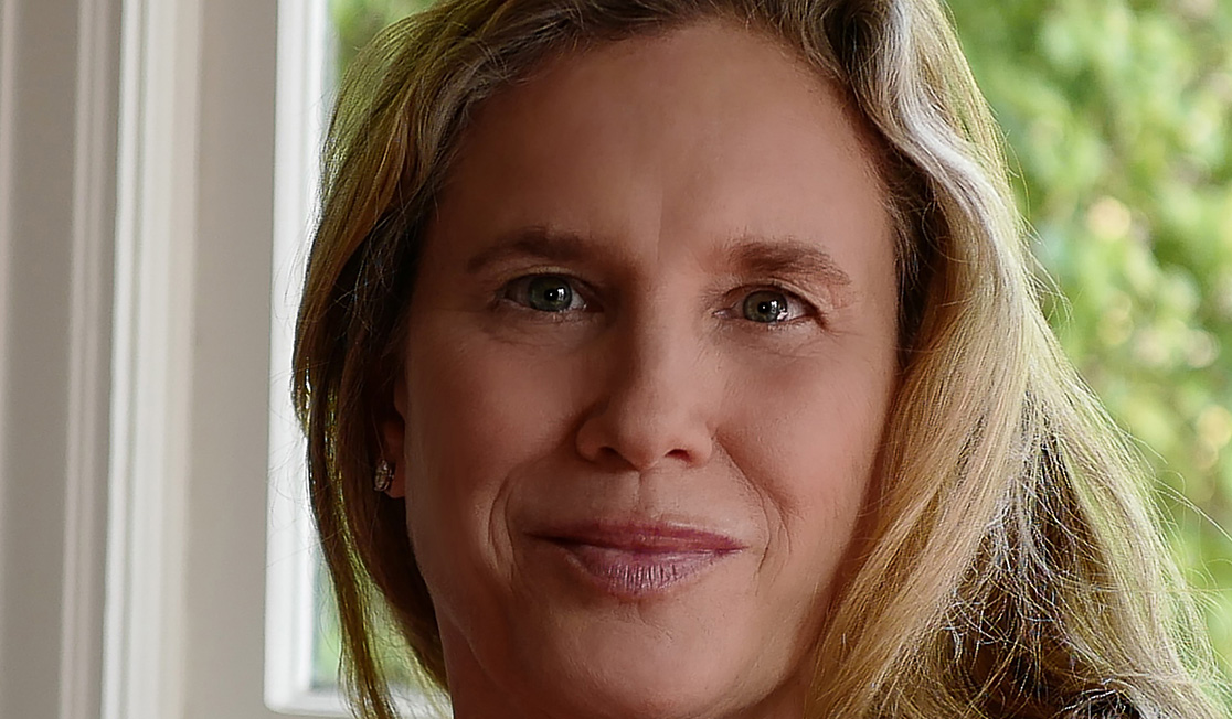 Miranda Cowley Heller is in front of a window. Miranda has blonde hair and smiles slightly.