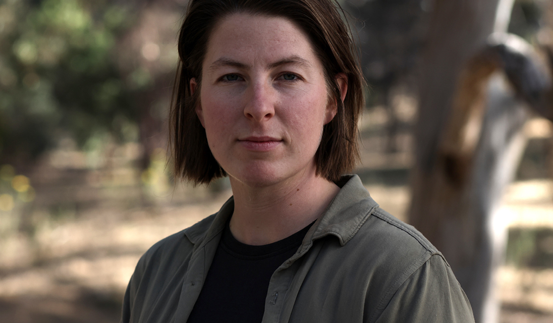 Lauren wears a dark green shirt with a black t-shirt underneath, she has short dark brown hair and looks directly at the camera