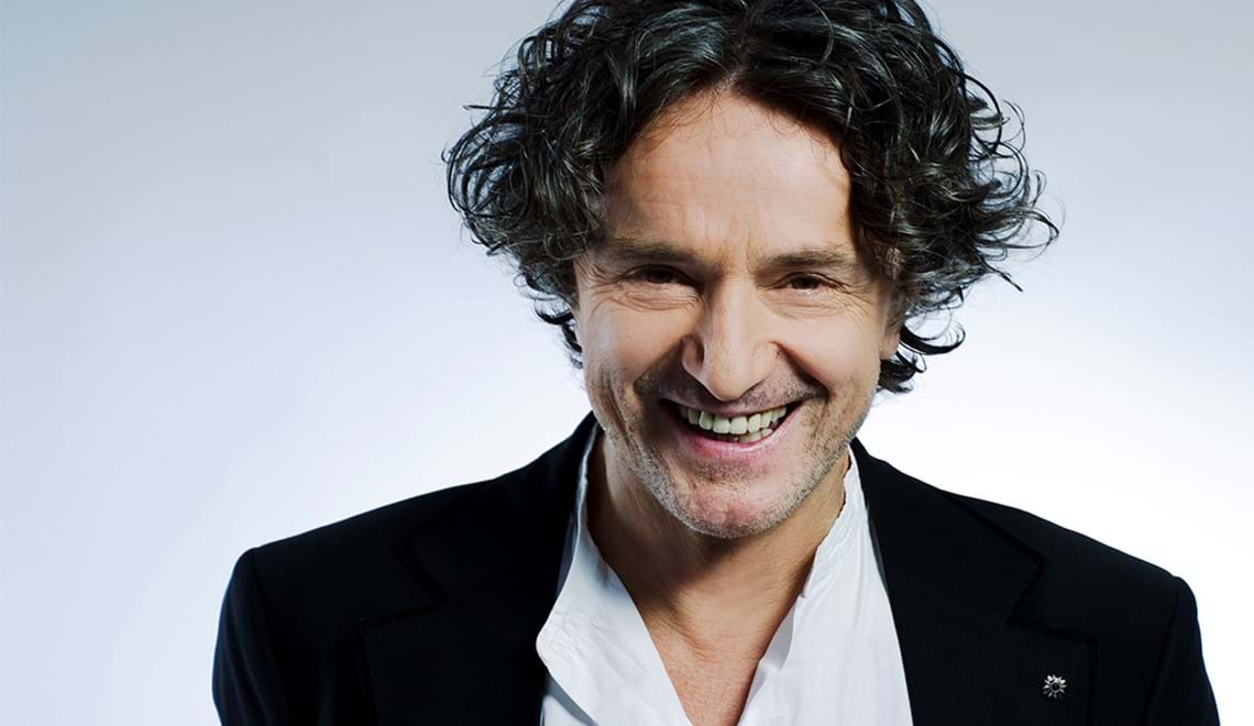 Goran smiles at the camera. He has curly black hair and is wearing a black suit jacket with a white shirt.