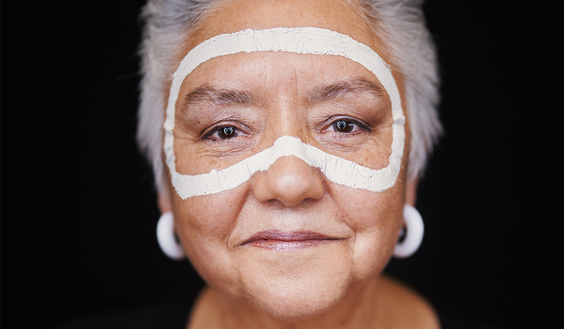 A close up of Lou Bennett wearing white earrings. She has a slight smile and short grey hair.