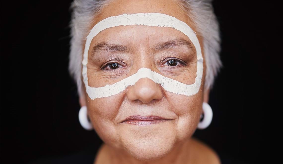 A close up of Lou Bennett wearing white earrings. She has a slight smile and short grey hair.