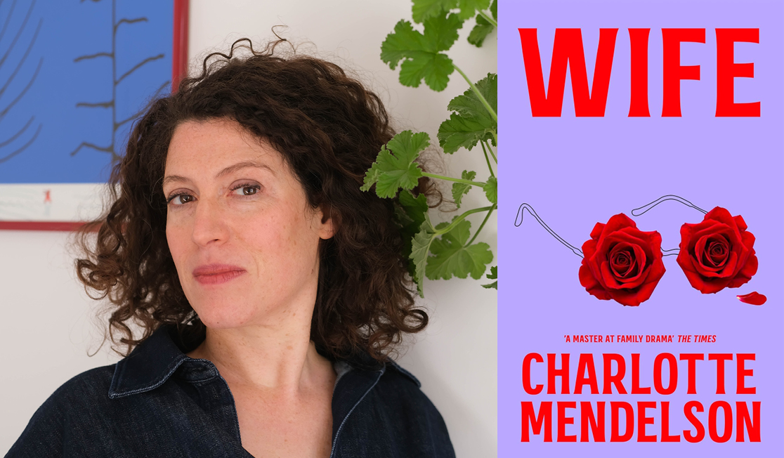 Charlotte Mendelson wears a collared shirt and stands in front of a white wall. Charlotte has curly brown hair.