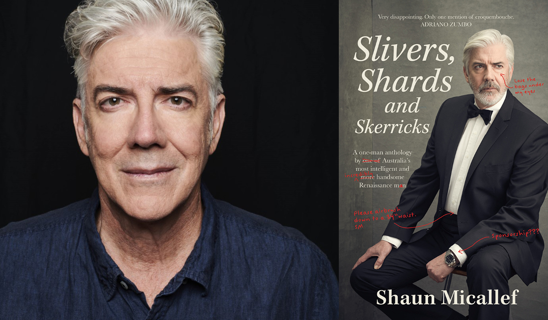 Shaun Micallef wears a blue shirt in front of a black background. Shaun has short grey hair and is slightly smiling.