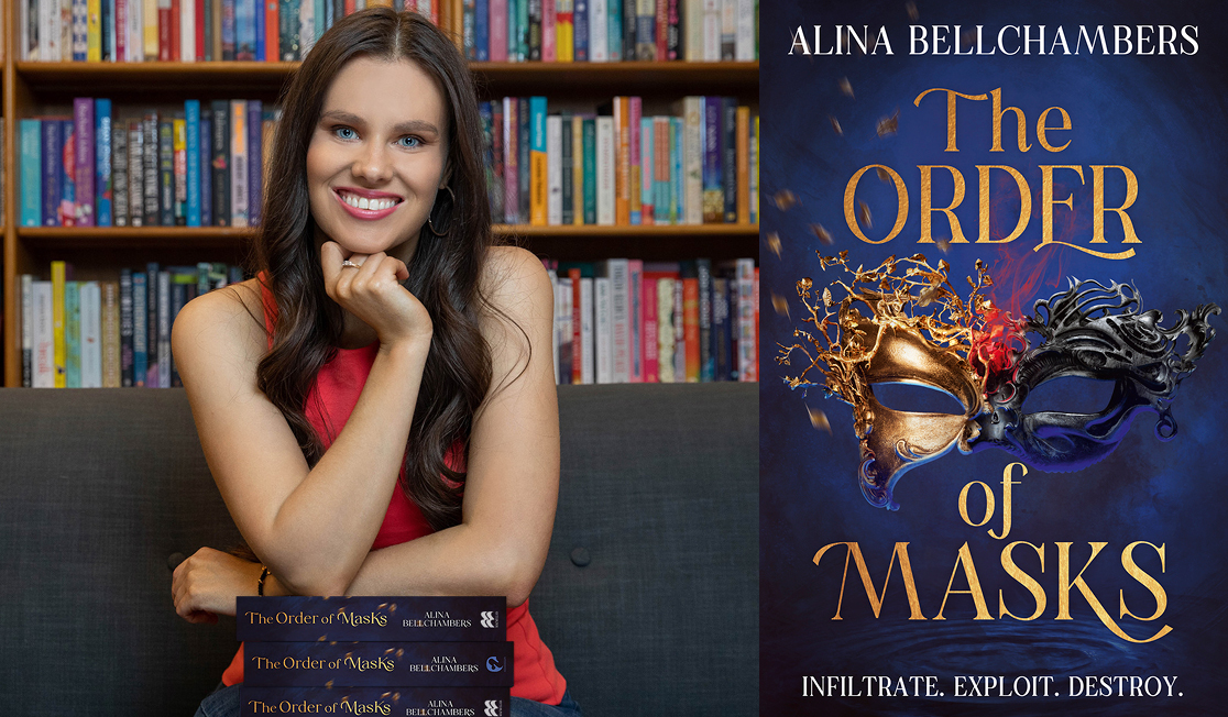 Alina Bellchambers wears a red dress and sits on a couch in front of a bookshelf. Alina has long brown hair and is smiling with one hand resting on their chin,