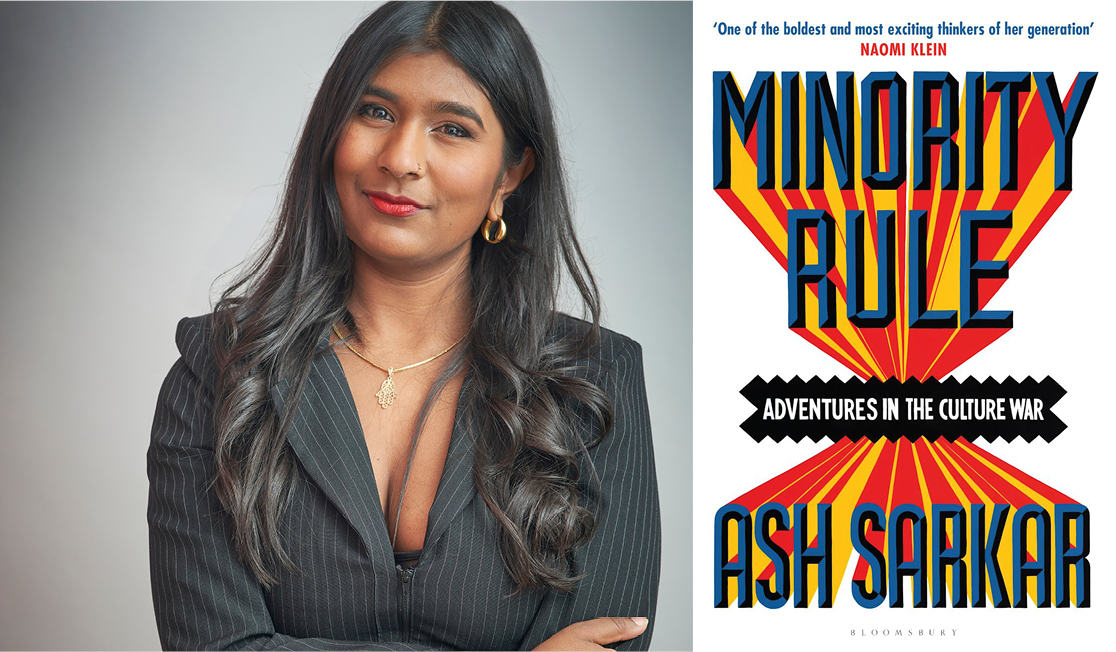 Ash wears a black blazer with gold jewellery. Ash has long wavy brown hair and is smiling.