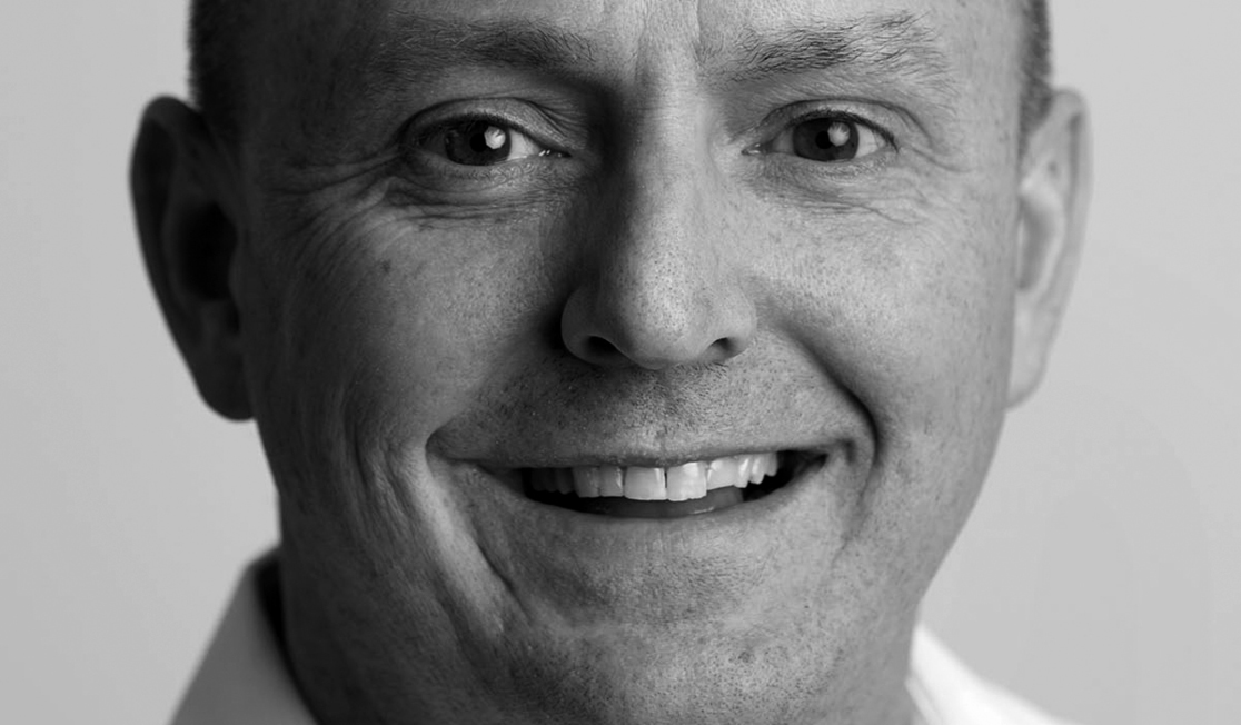 Close up of Richard Denniss in black and white. He wears a white collared shirt and smiles.