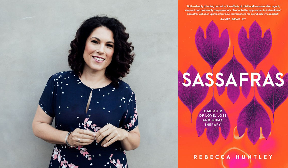 Rebecca Huntley stands in front of a grey wall wearing a blue top. Rebecca has dark curly hair and is smiling.