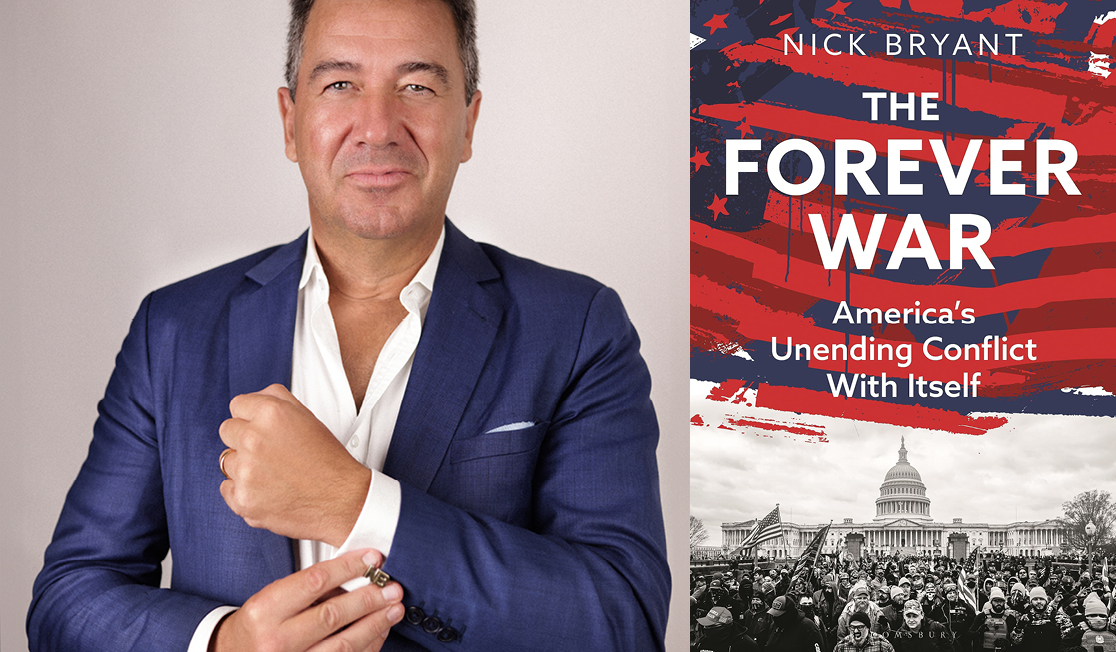 Nick Bryant stands in front of a light background wearing a blue suit jacket and a white shirt. He has both hands up, like he is adjusting his shift cuff.